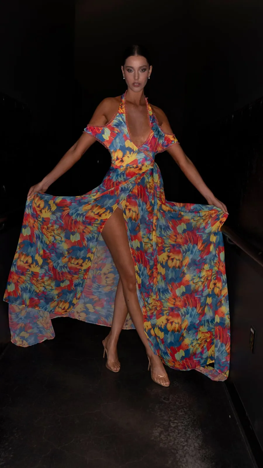 A model holding out a long floral cape backstage against a black wall