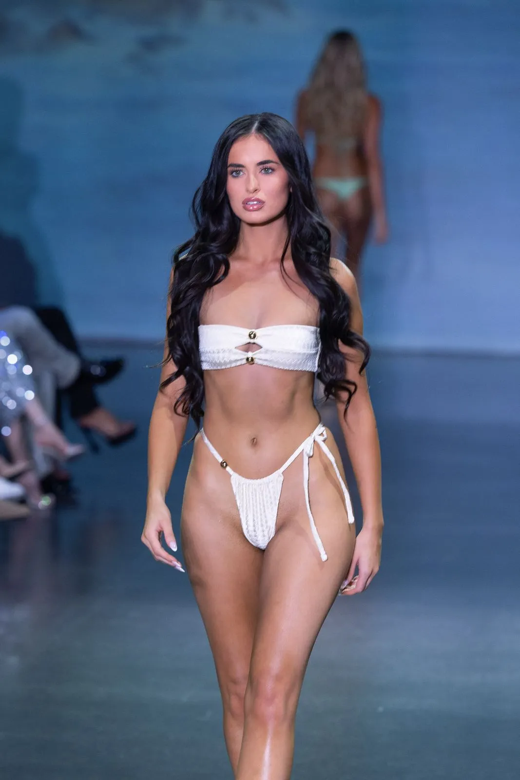 A model with long dark hair in a white tie-side bikini on the runway