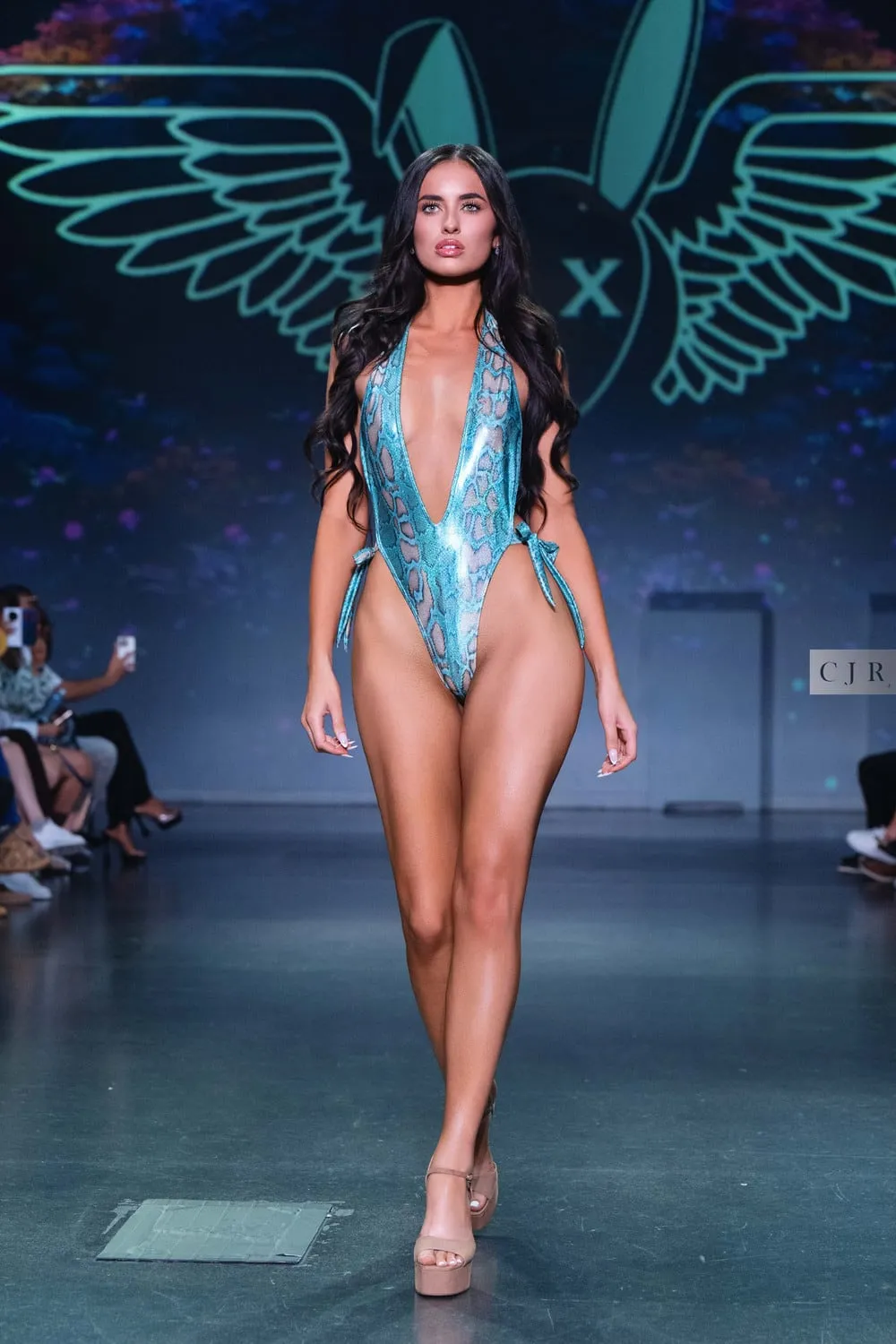 A model in a metallic teal plunging one-piece on the runway