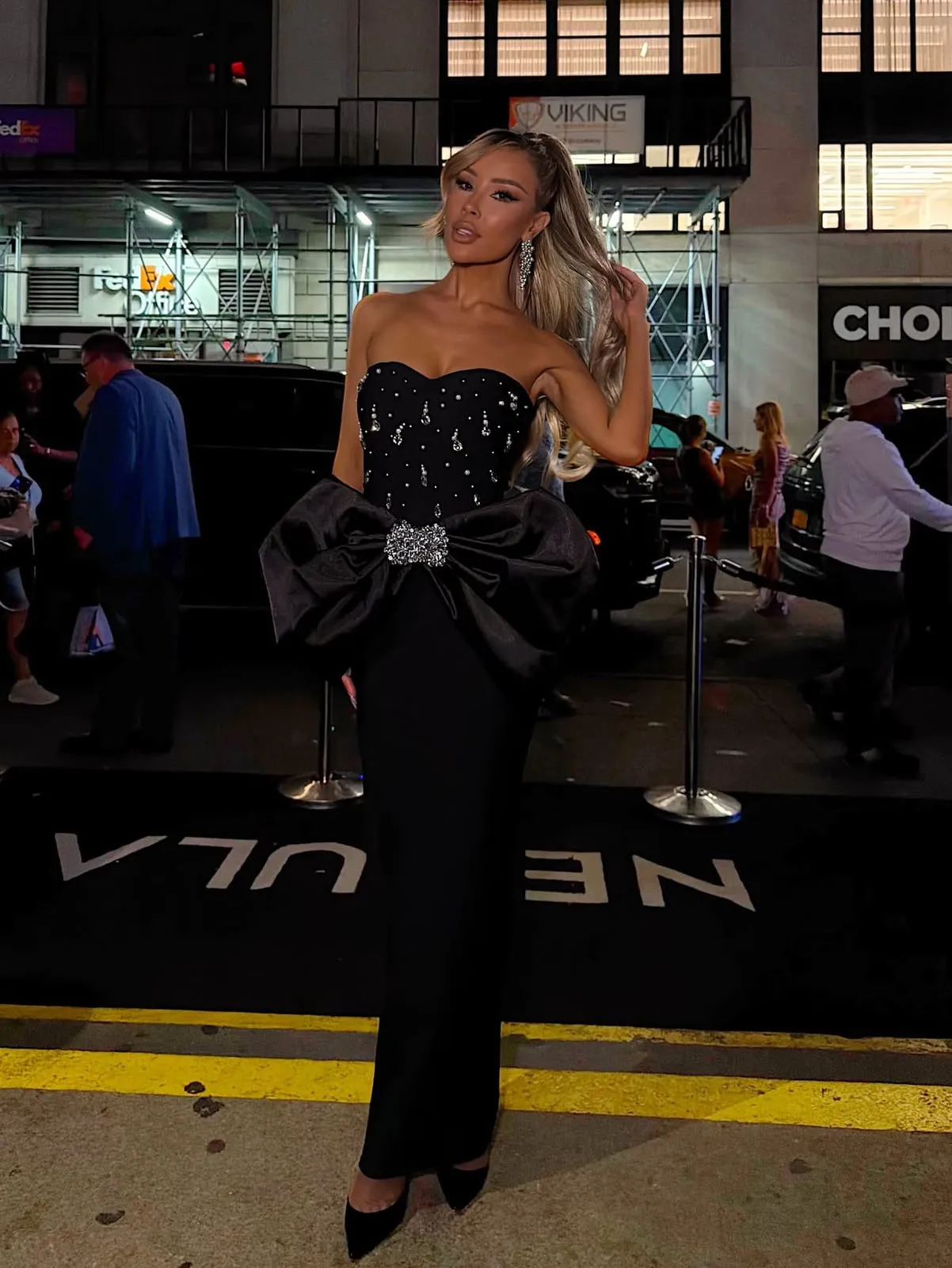 A model in a black strapless gown with an oversized bow on a city street at night