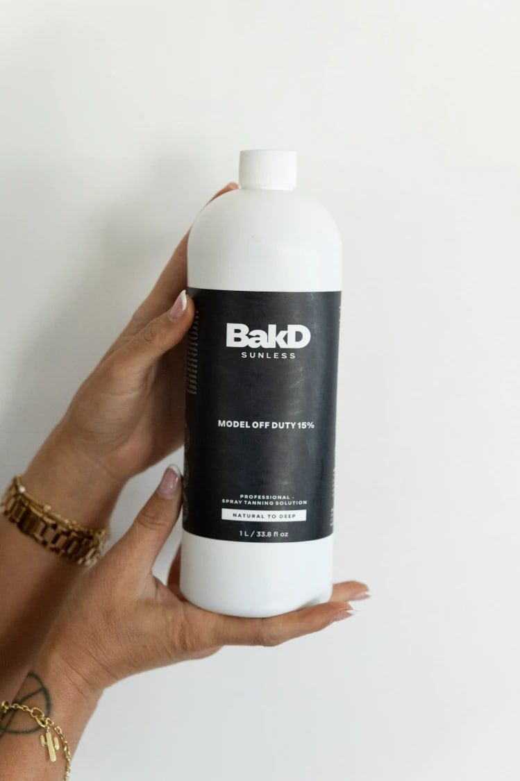 Hands holding a liter bottle of BakD Sunless Model Off Duty 15% professional spray tanning solution