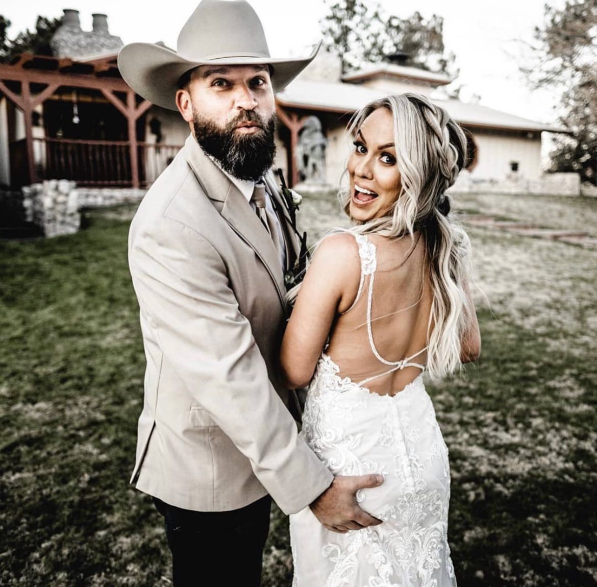 A groom in a cowboy hat and his bride in a lace gown laughing outdoors